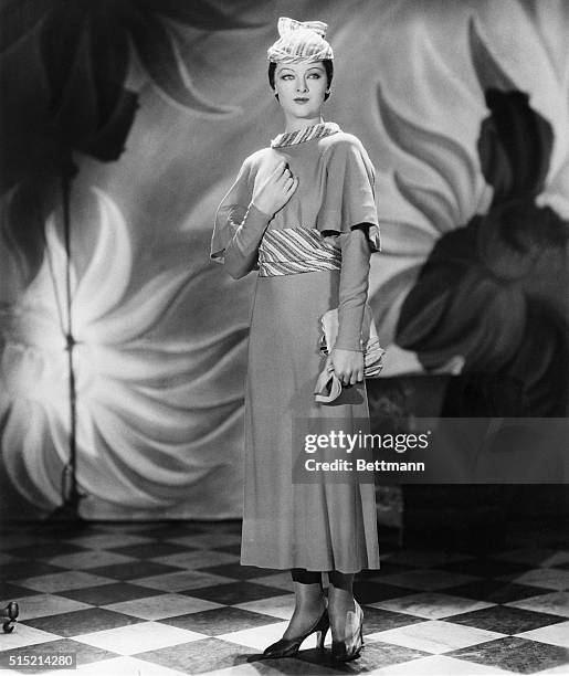 Chartreuse wool accented by trimming of vari-colored woven fabric forms this dress worn by Myrna Loy, RKO player. The hat is of the same material as...