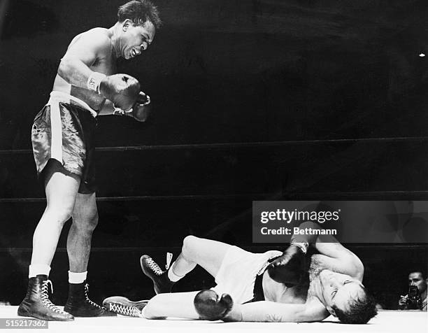 New York, NY- Light heavyweight champion Archie Moore stands over challenger Carl "Bobo" Olson after crashing him to the canvas in the third round of...