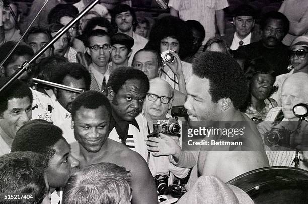 Uniondale, NY-A smiling Joe Frazier looks back at the scales upon which George Foreman is being weighed in at Nassau Coliseum today for their bout...