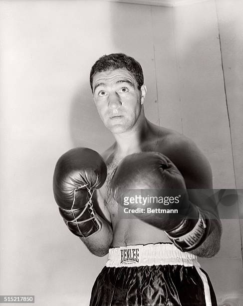Boxer Rocky Marciano poses for a studio portrait that depicts him in a menacing fight pose, boxing gloves ready for action.