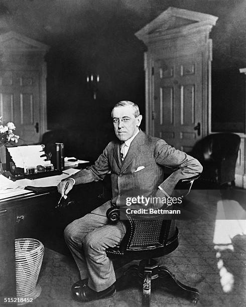 Portrait of Woodrow Wilson seated at his White House desk in 1919. He is turned toward the camera, holding a pen in hand.