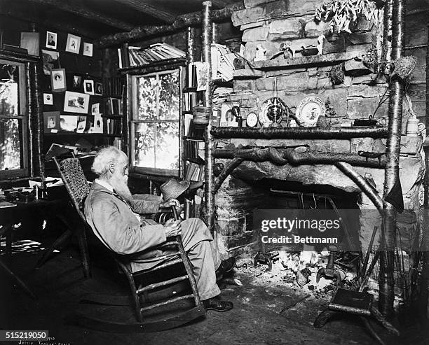 American naturalist John Burroughs seated in front of his fireplace. Photograph, 1910.