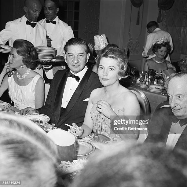 New York, NY: Cartoonist Charles Addams dips into a flaming "Zhonka" for actress Joan Fontaine at the annual Bal Blanc at the St. Regis Hotel.