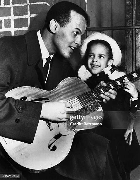 Harry Belafonte playing the guitar and holding his daughter Adrienne.