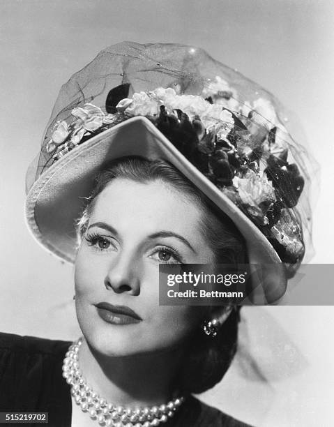 Hollywood, CA- A pastel felt bonnet topped with posies and jewel-dotted manline makes a lovely hat for actress Joan Fontaine. She will soon be seen...