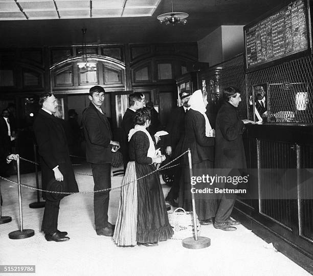 Immigrants standing in line in front of money exchange window on Ellis Island. Photograph, 1911.