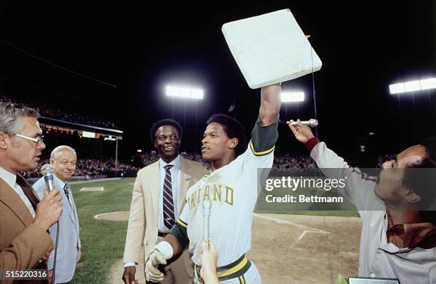 Oakland A's Rickey Henderson holds up the base as Lou Brock looks on after Henderson broke Brock's record on 118 steals by stealing his 119th in the...