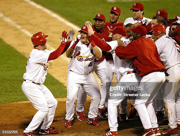 Jim Edmonds of the St. Louis Cardinals reaches home plate and his waiting teammates after hitting a two-run home run in the 12th inning to defeat the...