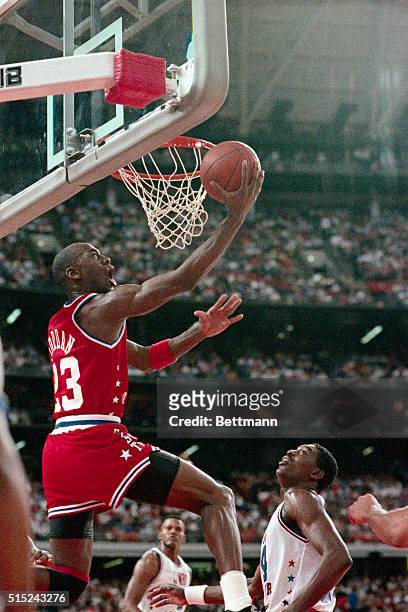 East's Michael Jordan of Chicago makes a reverse layup over the West's Akeem Olajuwon in the first quarter of the NBA All-Star game, 2/12. West's...