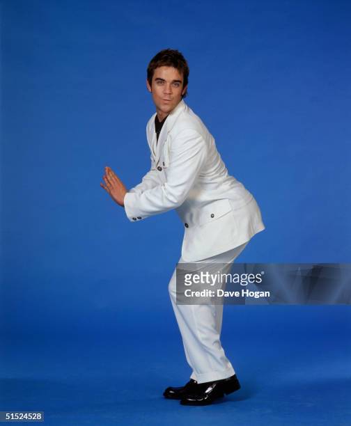 Pop singer Robbie Williams, member of boy band Take That, posing against a bright blue background, he is wearing a white suit, mid 1990s