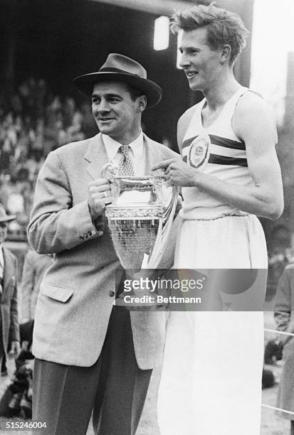 Philadelphia, PA- British Miler, Roger Bannister,, holds the Winner's Cup after turning in a fast 4:08.3 to easily win the Benjamin Franklin Mile of...