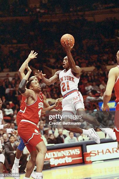 New York: Gerald Wilkins , of the N.Y. Knicks, goes airborne as he soars for the basket over two grounded Seventy-Sixers during their NBA game....