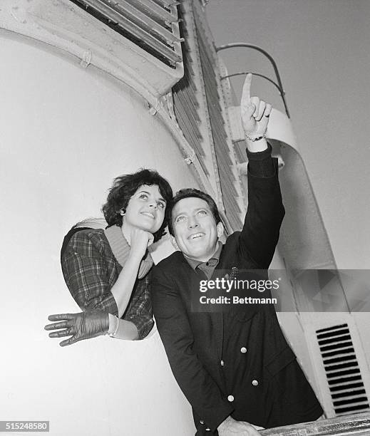 Singer Andy Williams points while standing with fiancee Claudine Longet, who is looking out from a porthole.