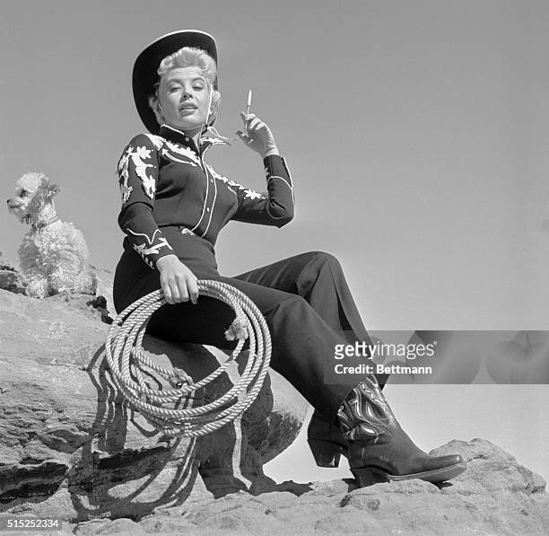 Fancy togs, a silver cigarette holder and a French poodle make a sophisticated cowgirl of actress Gloria DeHaven. On location at Las Vegas, Gloria...