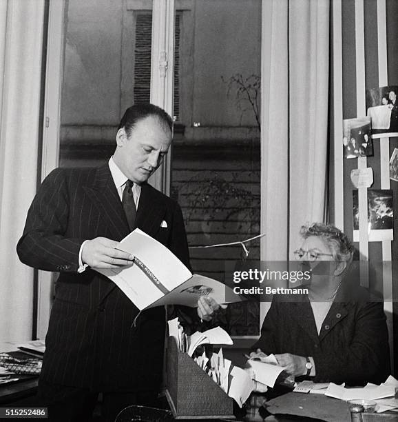 Parisian designer Pierre Balmain is shown with his assistant, looking at book designs by Marcel Rochas.