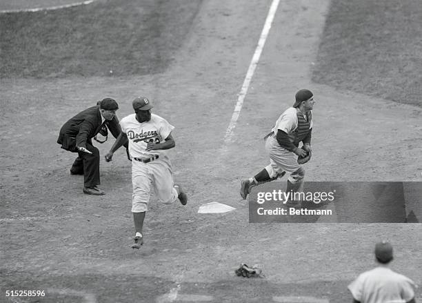 Brooklyn's Jackie Robinson, coming home from 3rd on teammate Roy Campanella's 3rd inning left-field fly is safe at the plate as he evades Milwaukee...