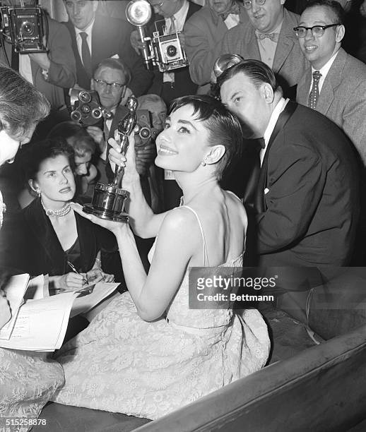Audrey Hepburn, surrounded by photographers and reporters, holds up the Academy Award she won for best actress in Roman Holiday, her first American...