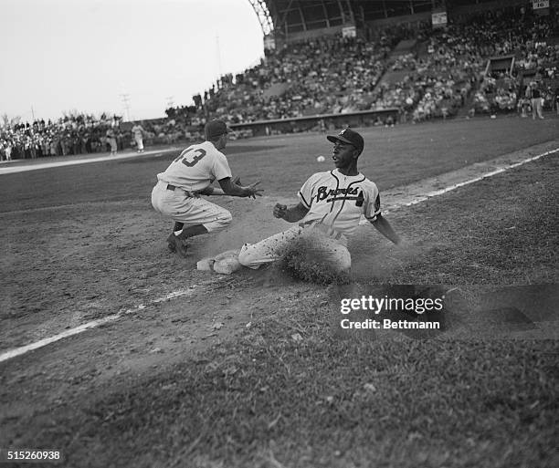 Hank Aaron, Milwaukee Braves' outfielder, gets back to third safely, sliding into base during exhibition game with Brooklyn Dodgers. The ball got...