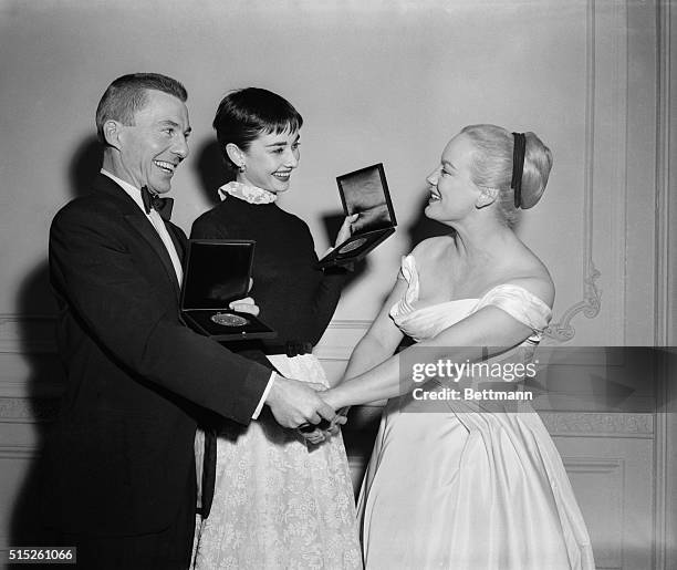 Actress Faye Emerson, , gives this year's "Tony" winners, David Wayne, and Adurey Hepburn, a warm handshake, after receiving their awards. Audrey won...