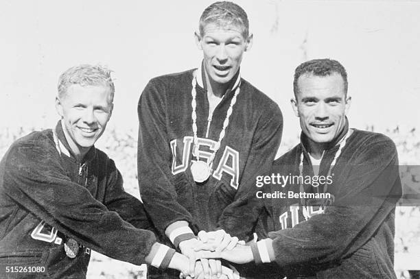 Clasping hands after finishing one-two-three in the Olympic 40-meter hurdles, U.S. Track stars stand on the podium 9/2. Left to right are: Cliff...