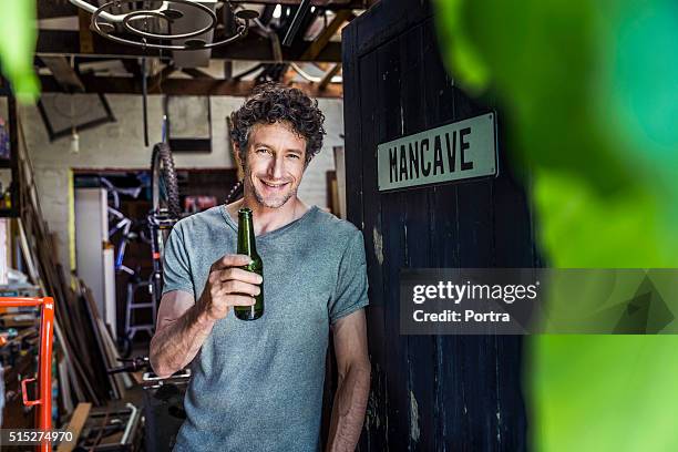 happy worker holding beer bottle in workshop - man cave stock pictures, royalty-free photos & images