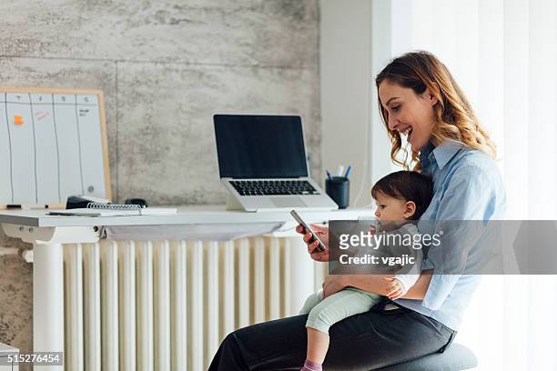 madre trabajando desde casa y agarrando su bebé - leanincollection working mom fotografías e imágenes de stock