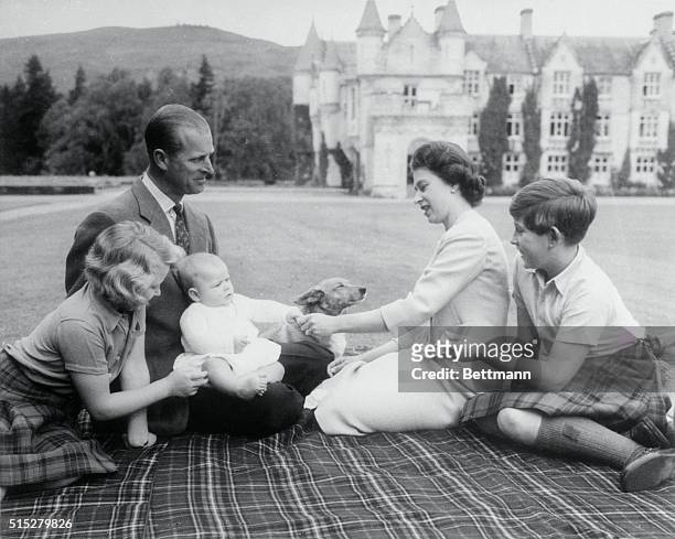 Baby Prince Andrew perches on Prince Philip's lap during a picnic on the grounds of Balmoral Castle. Looking on are Queen Elizabeth, Prince Charles,...