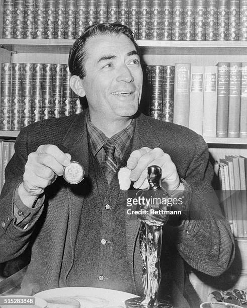 Gregory Peck has breakfast in the "company" of his "Oscar" April 9th. Peck holds a rabbit's foot and a gold watch. His daughter Cecilia gave him the...