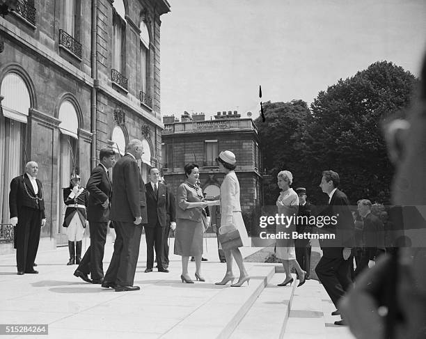 While Palace Guards raise their sabres in salute, Madame Yvonne de Gaulle welcomes Mrs. Jacqueline Kennedy to Elysee Palace here May 31st. Looking on...