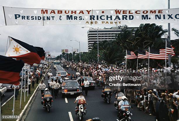 Surrounded by flag-waving crowd, President Richard Nixon and Philippines President Ferdinand E. Marcos wave from car during motorcade to Malacanang...