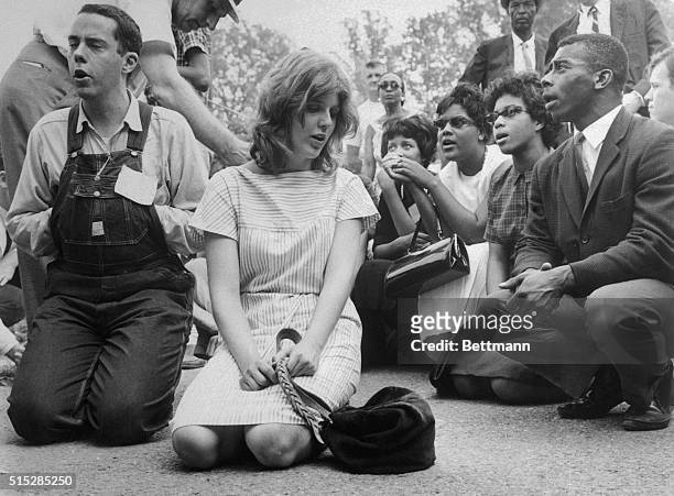 These pickets kneel on pavement and sing songs as they await police buses after their arrest on trespassing charges during segregation demonstration...