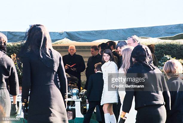 In this photo the Kennedy family is shown at a committal service for Joseph P. Kennedy. The girl who is turned around looking at the camera is a...