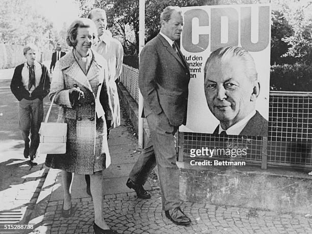 "The Grand Coalition" Bonn: Returning home after voting, West German Foreign Minister Willy Brandt walks past a large campaign poster right in front...