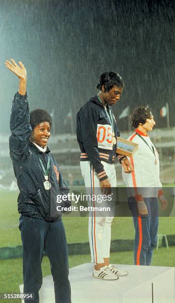 Mexico City, Mexico: Wyomia Tyus of the U.S., first place winner in the 100 meter dash, stands in the rain and walks off the field with her two...