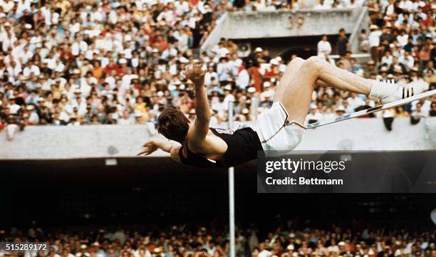 Richard Fosbury of the U.S., in his unusual "flip-flop" style, sets an Olympic record as he clears the bar in the high jump event at 7 feet, 4 1/2...