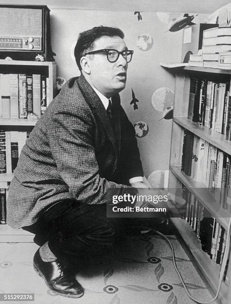 Biochemist and Science Fiction novelist Isaac Asimov squatting near a bookshelf.