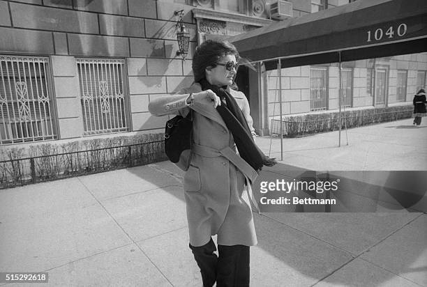 Recently widowed Jacqueline Onassis turns her head and raises her arm to avoid a photographer as she leaves her New York apartment.