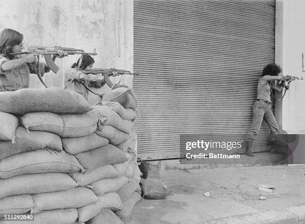 Teenage Christian girls, all members of the right wing Phalangist Party, man a sandbagged barricade and point their guns down a street in downtown...