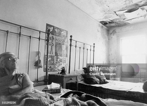 Mrs. Edith Beale lies in bed near crumbling ceiling in room of run down 28 room mansion here. Papers protect her bed.