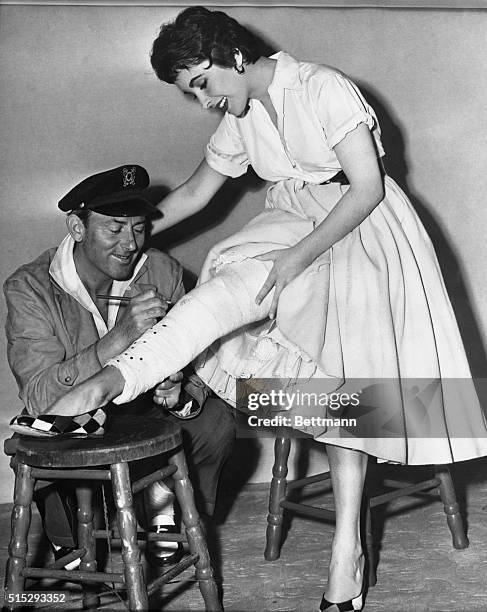 Husband Michael Wilding autographs Liz Taylor's cast which was placed on the movie actress' leg after she injured the limb getting out of a car. The...