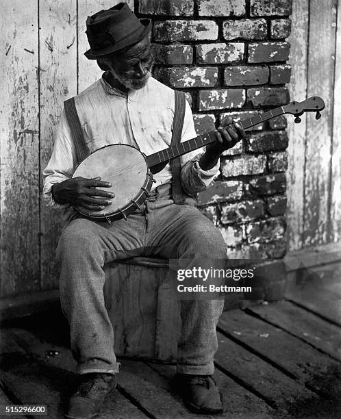 An elderly African American man plays his banjo on his front porch.