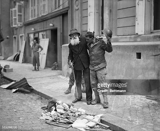 Cherbourg, France- A doughboy removes his tin derby in mock reverence as a Nazi swastika flag burns in a gutter in Cherbourg while an armed Frenchman...