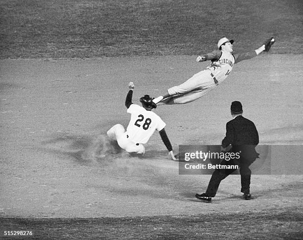 Los Angeles, CA- Cincinnati Reds' second baseman Pete Rose leaps high in the air to grab a high throw from catcher John Edwards, as Dodger Wes Parker...