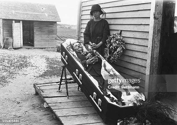 Near Albany, Minnesota: A widow poses on the porch of a farm house, beside the open coffin of her dead husband. She is shown standing behind the...