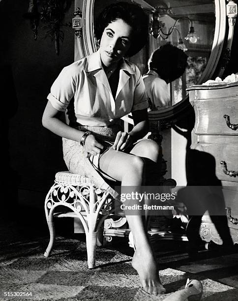 Elizabeth Taylor in a scene from the 1958 MGM release "Cat on a Hot Tin Roof." She is shown seated in a bedroom, unfastening her garter belt.