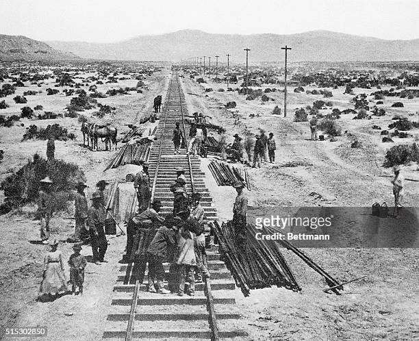 Working in the shimmering heat, rail layers are shown laying down track in Nevada as the Central Pacific forces worked eastward. A telegraph line...