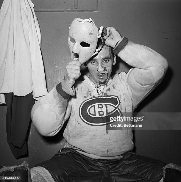 New York, NY- His face and shirt bloodied, Montreal Canadiens goalie Jacques Plante puts on a special plastic mask after being treated for a facial...