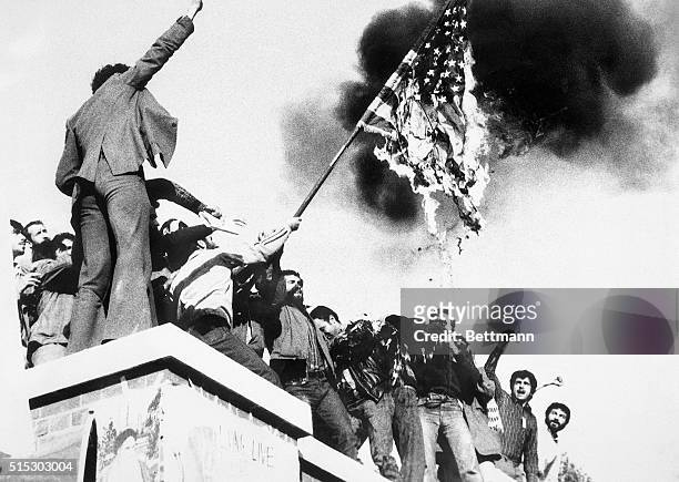 Teheran, Iran: Demonstrators perched atop of the United States Embassy wall, burn an American flag, the fourth American flag to be burned since the...