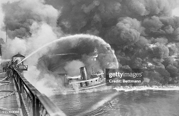 Cleveland,OH- Firemen stand on a bridge over the Cuyahoga River to spray water on the tug Arizona, as a fire, started in an oil slick on the river,...