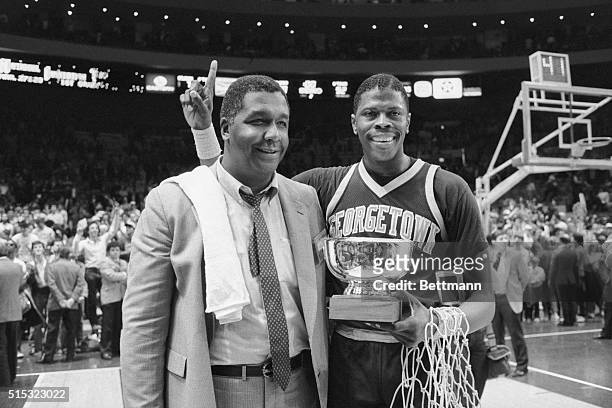 New York: Georgetown's Most Valuable Player, Patrick Ewing, holds his MVP trophy and victory net as he gives the sign behind coach John Thompson...